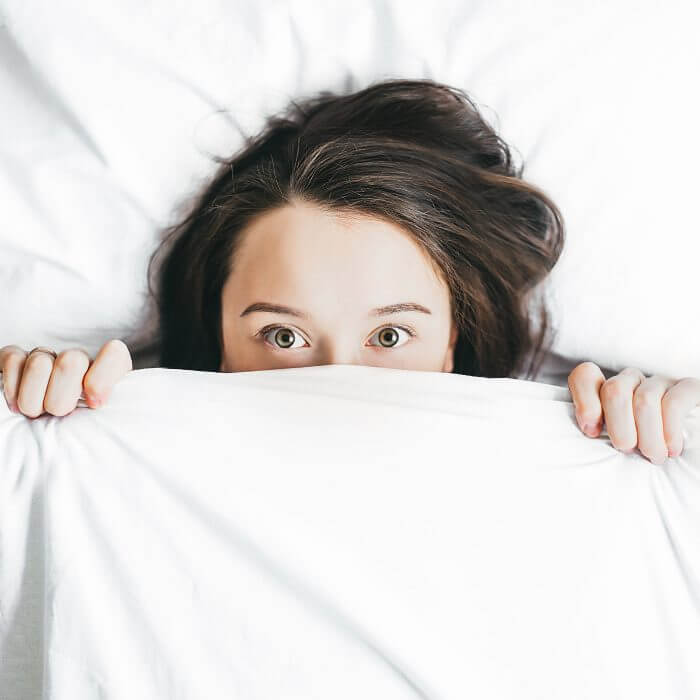 woman with acne hiding under the covers