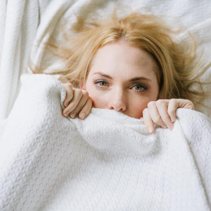 picture of a woman with acne hiding her face under the covers