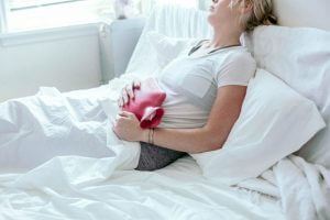 picture of a woman with a hot water bottle over her abdomen because of bad menstrual cramps or dysmenorrhea
