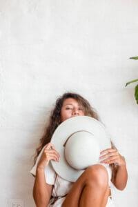 picture of a woman holding a hat up to her face to hide her acne prone skin due to hormonal imbalance wondering about the causes of acne