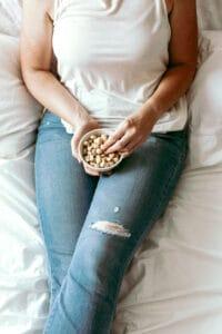 picture of a woman lying on her bed healthy snacking on nuts with mindfulness for weight loss, thinking about other healthy snacks