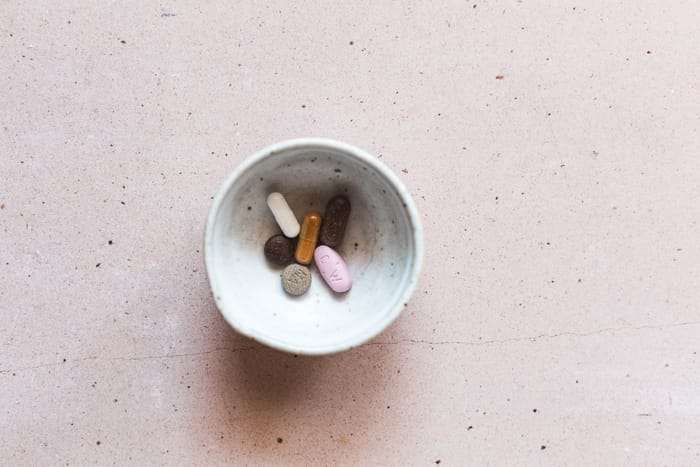 Glutathione: What It Is and Why It Matters picture of a bowl with glutathione supplements, vitamin C, vitamin E, and liver detoxification supplements in it on a pink background