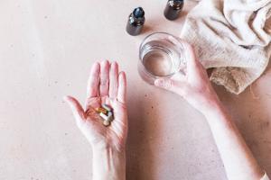 Endocrine Disrupting Chemicals and Hormone Imbalance picture of a glass of water and a hand holding pills to detox endocrine disrupting chemicals